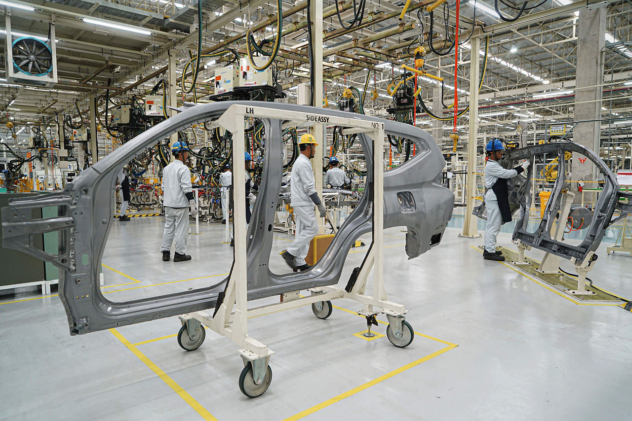 A car body part at the Mitshubishi plant in Indonesia. Behind them, workers at the assembly stations.