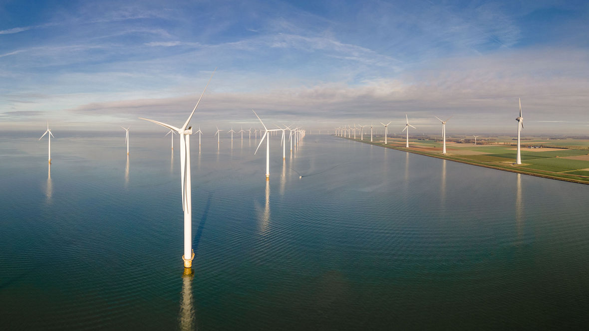 Large wind turbines installed in the sea and along the coastline under a blue sky, representing renewable energy generation from wind power