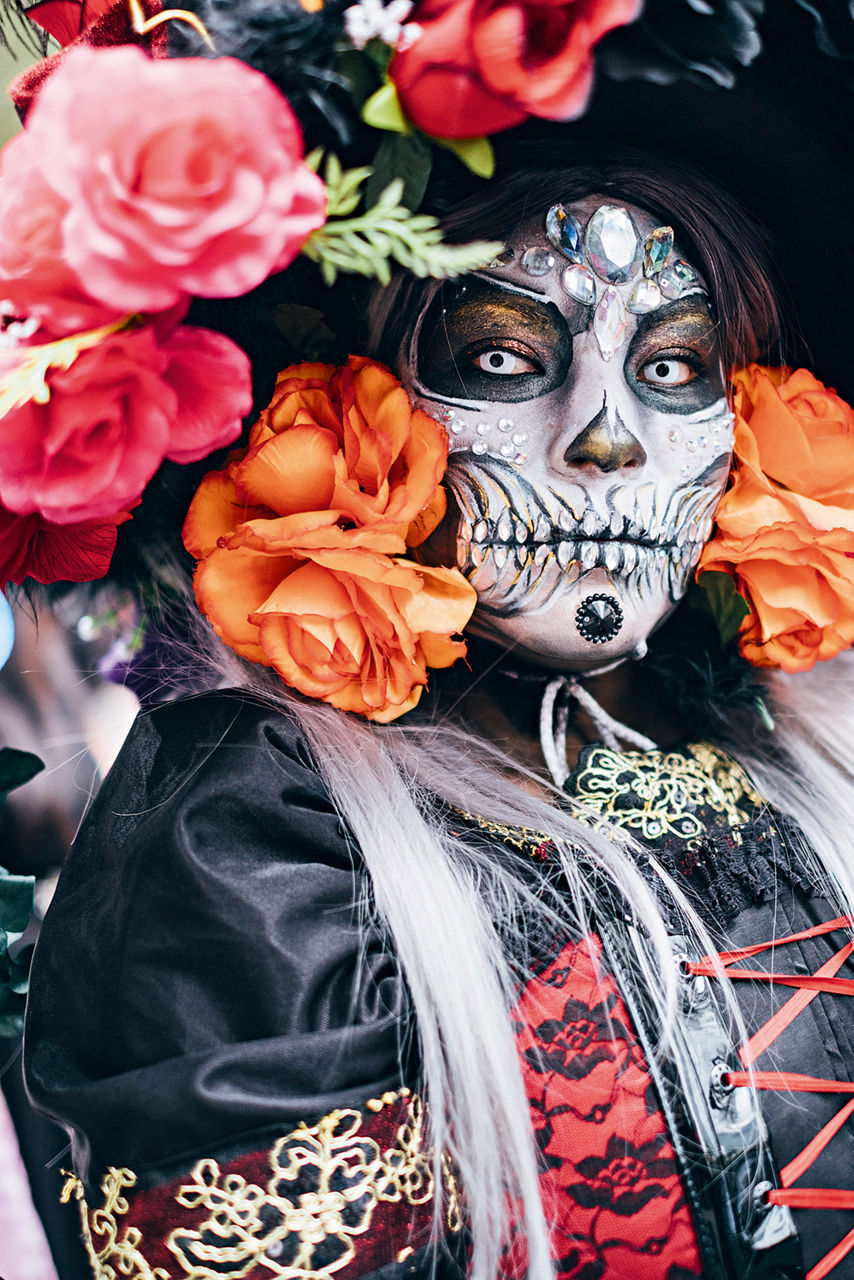 Eine Frau hat sich am Tag der Toten kunstvoll zu einem Skelett geschminkt. Sie trägt Seidenblumen im Haar und einen dunklen Umhang.