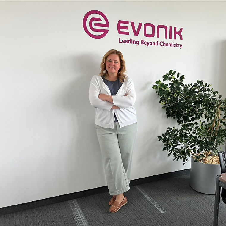 Person standing with arms crossed near a large potted plant in a modern office space.