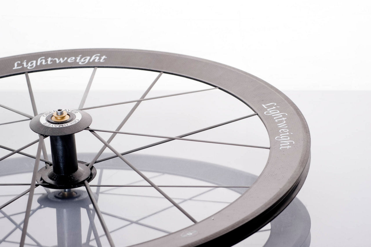 Carbon fiber bicycle wheel with thin spokes and "Lightweight" printed on the rim.