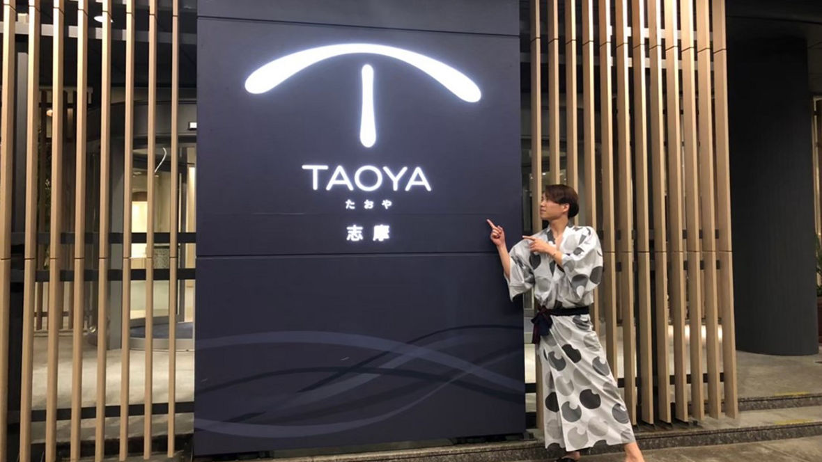 A person in a traditional yukata poses next to the TAOYA logo at a modern entrance.