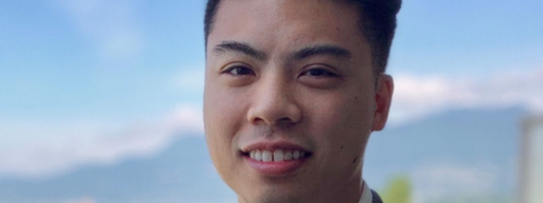 Ein Mann in einem grauen Anzug steht im Freien mit einer schönen Berglandschaft im Hintergrund.