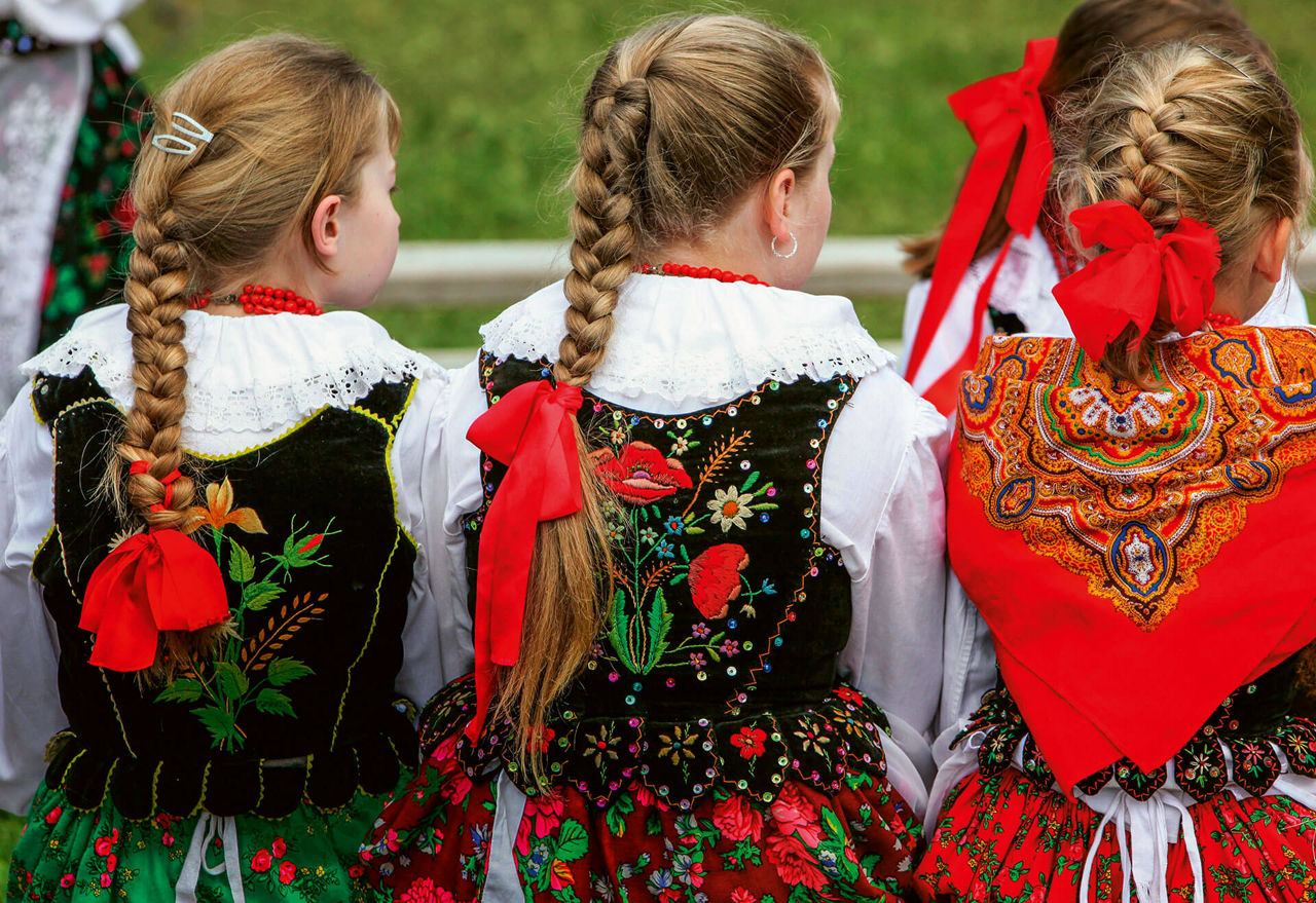Junge Mädchen von hinten gesehen. Sie tragen schwarz, grün, rote Trachten mit Stickereien.