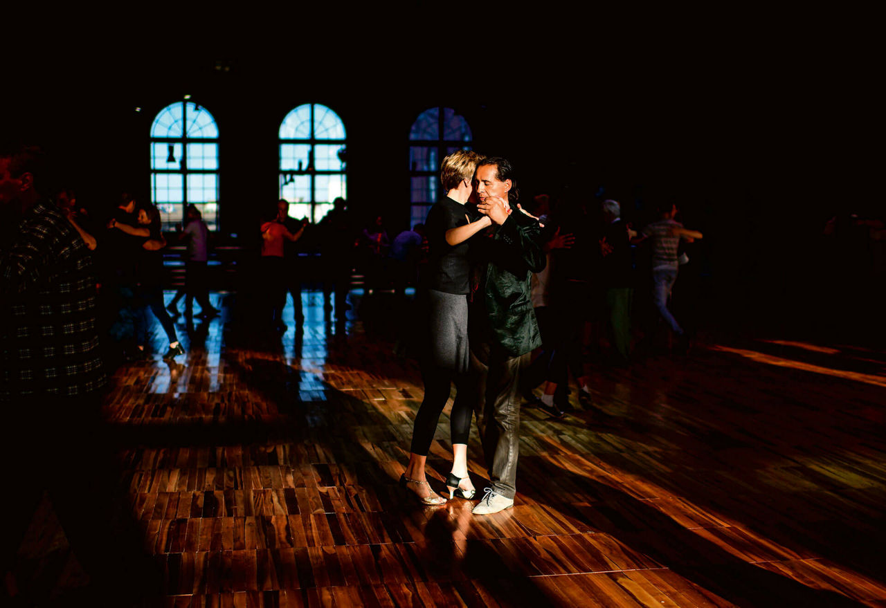 Tangotänzer in einem großen Saal mit glänzendem Holzboden.
