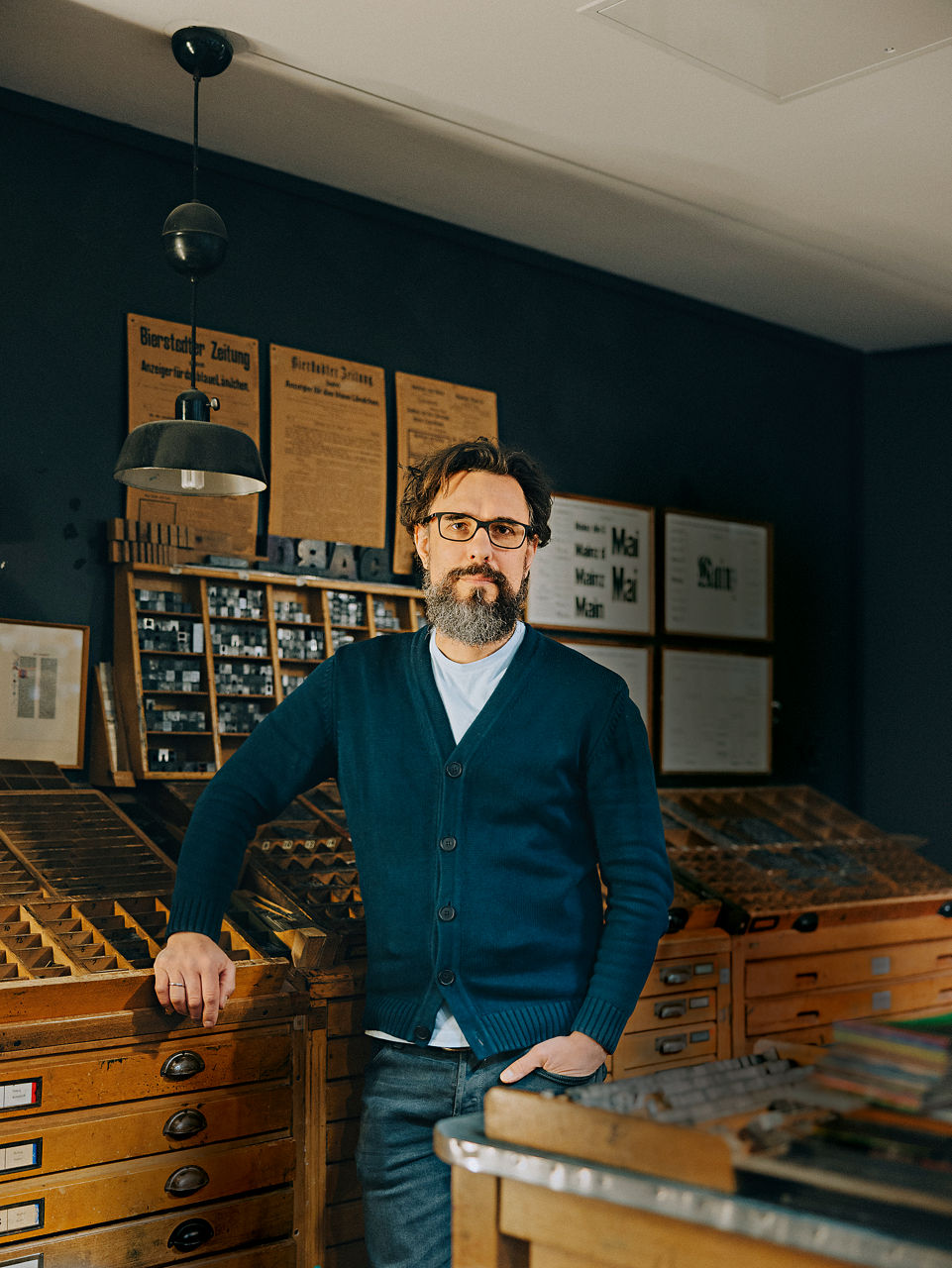Christoph Sünder leans against a wooden shelf with movable type.