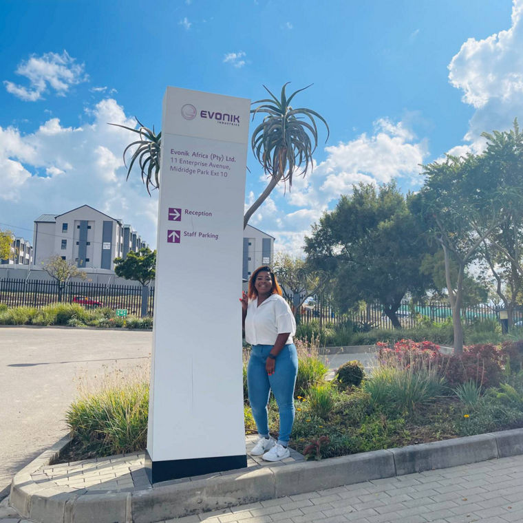 A woman stands beside a sign for Evonik Africa, indicating reception and staff parking.