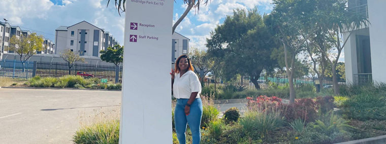 A woman stands beside a sign for Evonik Africa, indicating reception and staff parking.