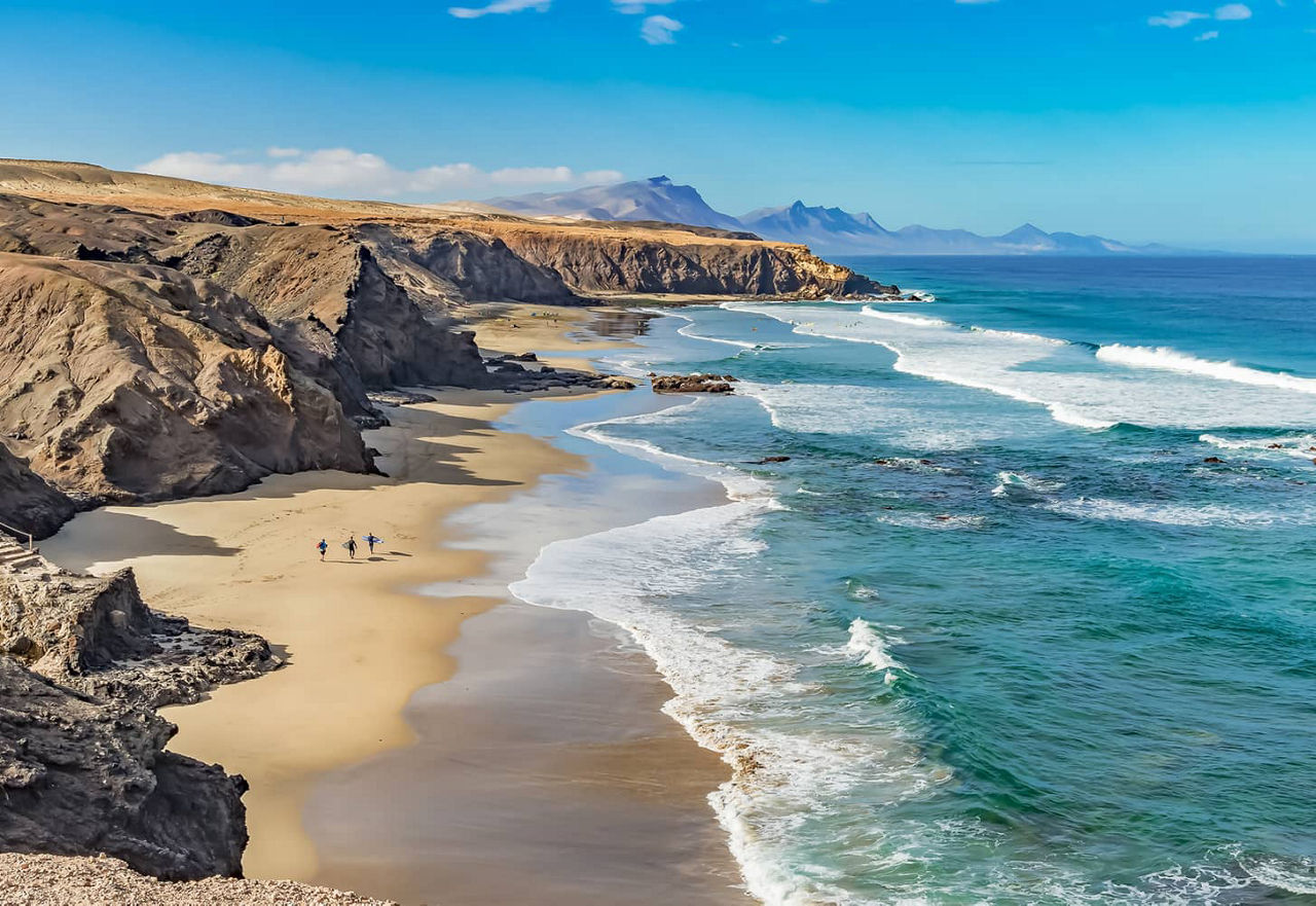 Three surfers walk along the beach
