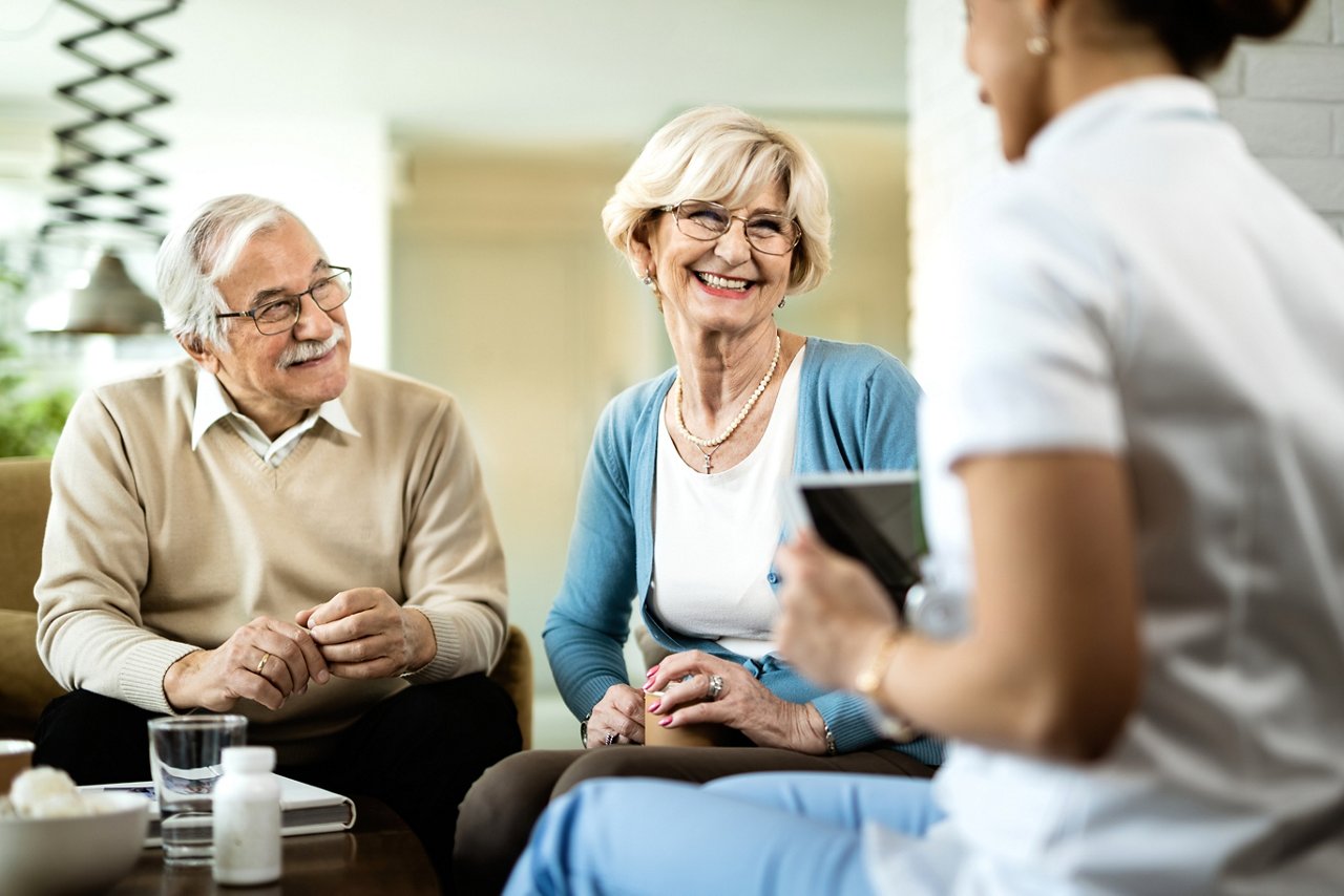 Happy senior couple and healthcare worker communicating during home visit.