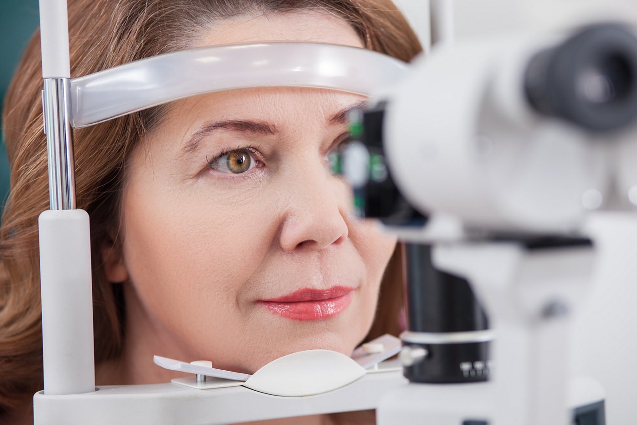 Pretty woman is looking into eye test machine with concentration in oculist lab. Focus on her face