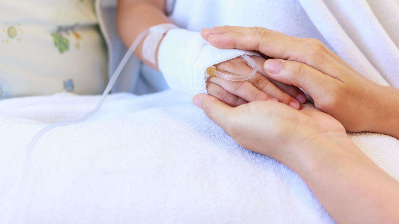 Close up hand of parent holding hand of child in hospital. 