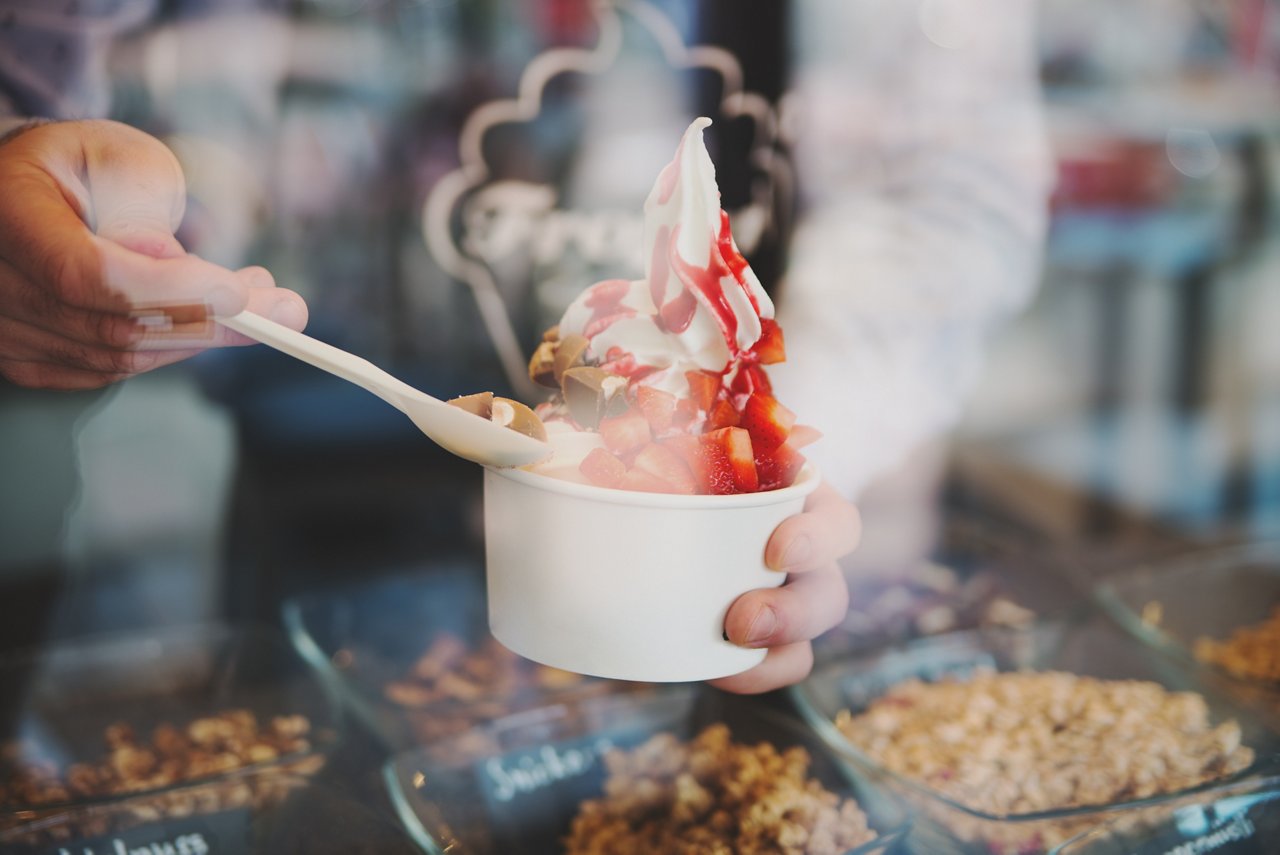 seller pours sauce on a soft frozen yogurt in wite take away cup in cafe