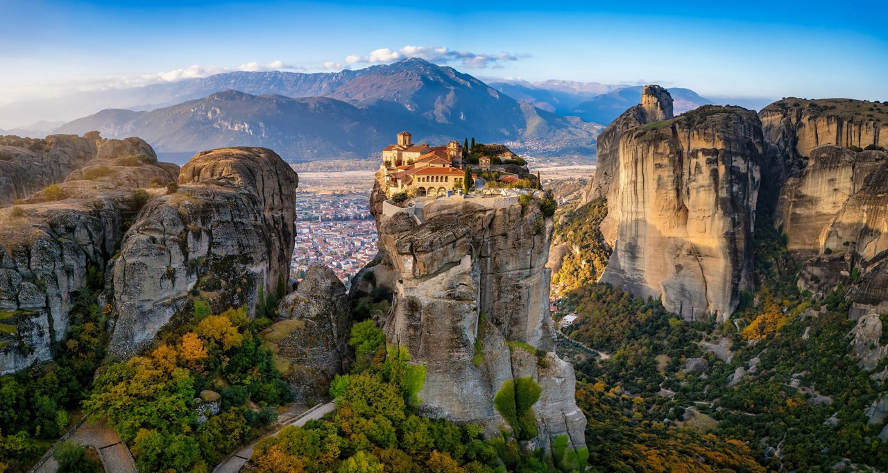 Panoramablick auf den Sonnenaufgang aus der Luft auf die Meteora-Berge mit dem Kloster Agia Triada auf einer Klippe hoch über dem Tal, Griechenland