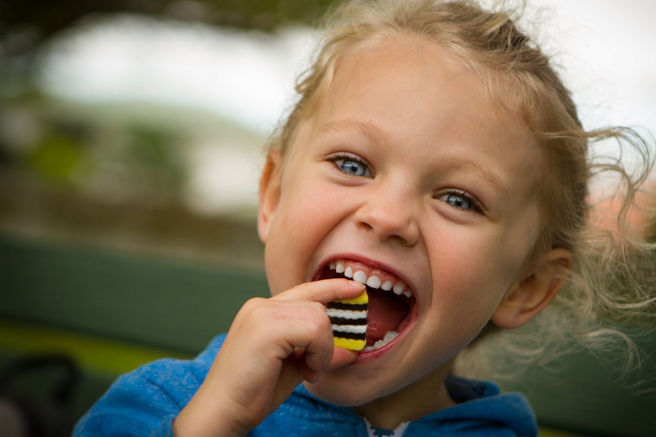 close up of a youngblonde haired blue eyed child with mouth wide open about to eat a large sweet.