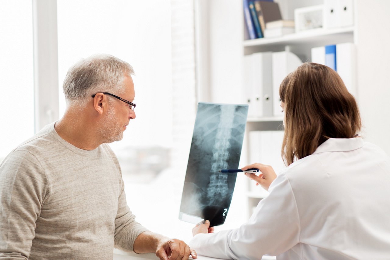 Arzt zeigt einem älteren Mann im Krankenhaus eine Röntgenaufnahme der Wirbelsäule.