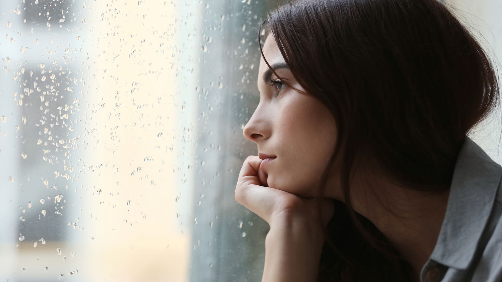 Depressed young woman near window at home, closeup
