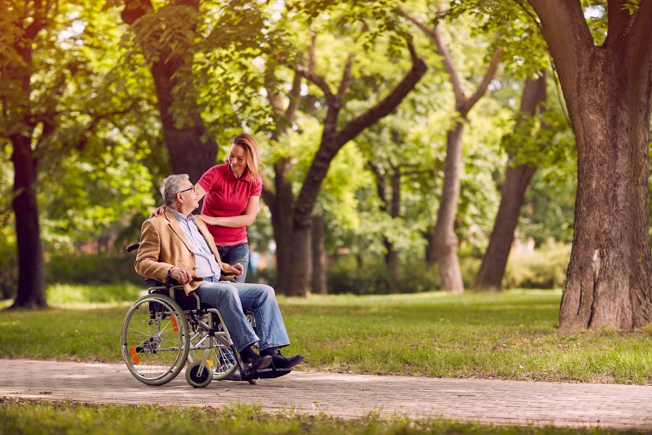  Glücklicher älterer Mann im Rollstuhl im Park mit lächelnder Tochter im Park