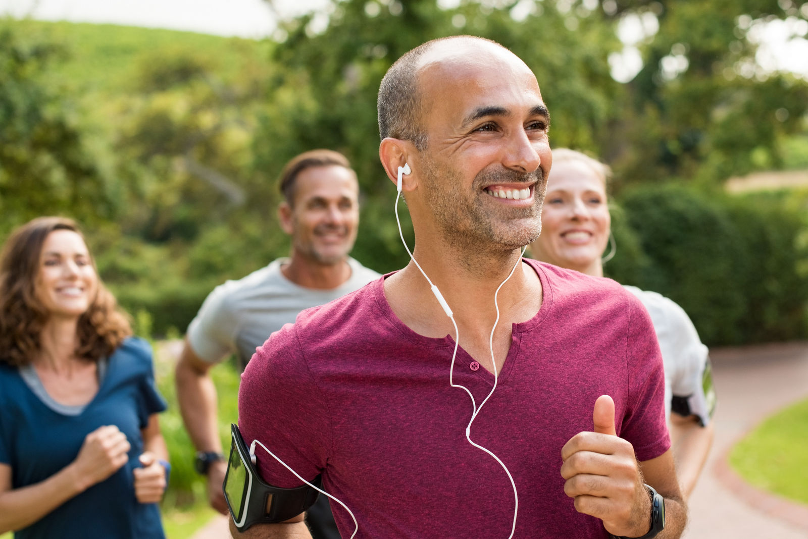 Portrait of a happy cheerful man listening to music while jogging. Man listening to music while jogging with group. Happy trainer in park running with team.