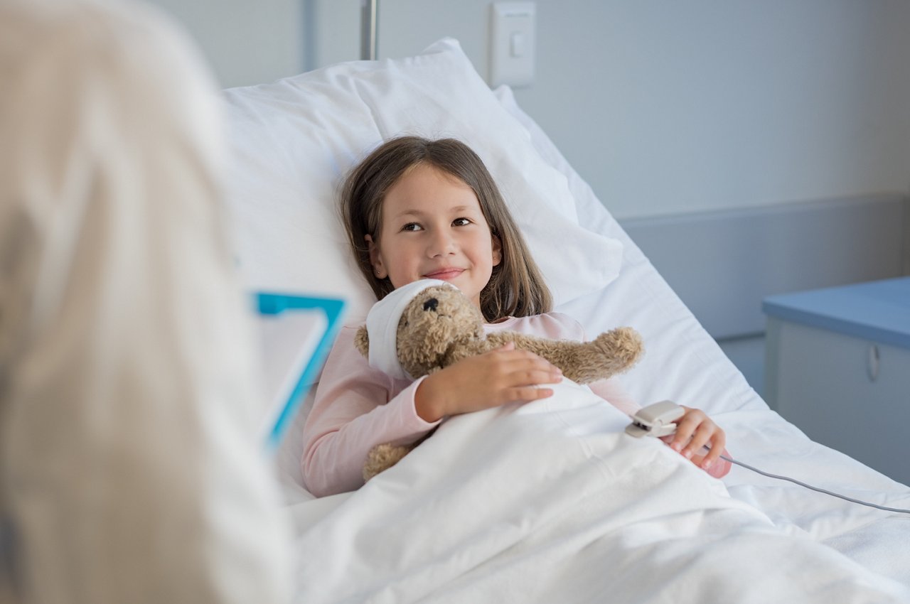 Smiling little girl with oxygen saturated probe resting on hospital bed. Girl patient looking at doctor with a smile. Child and doctor at medical clinic.