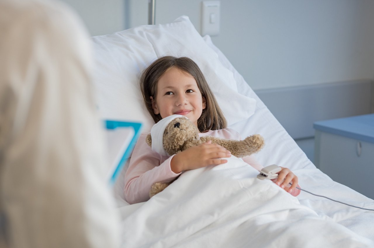 Süßes Mädchen liegt im Krankenbett mit einem Taddy im Arm
