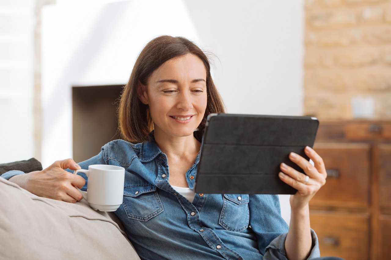 Mature woman using tablet computer while relaxing on sofa at home