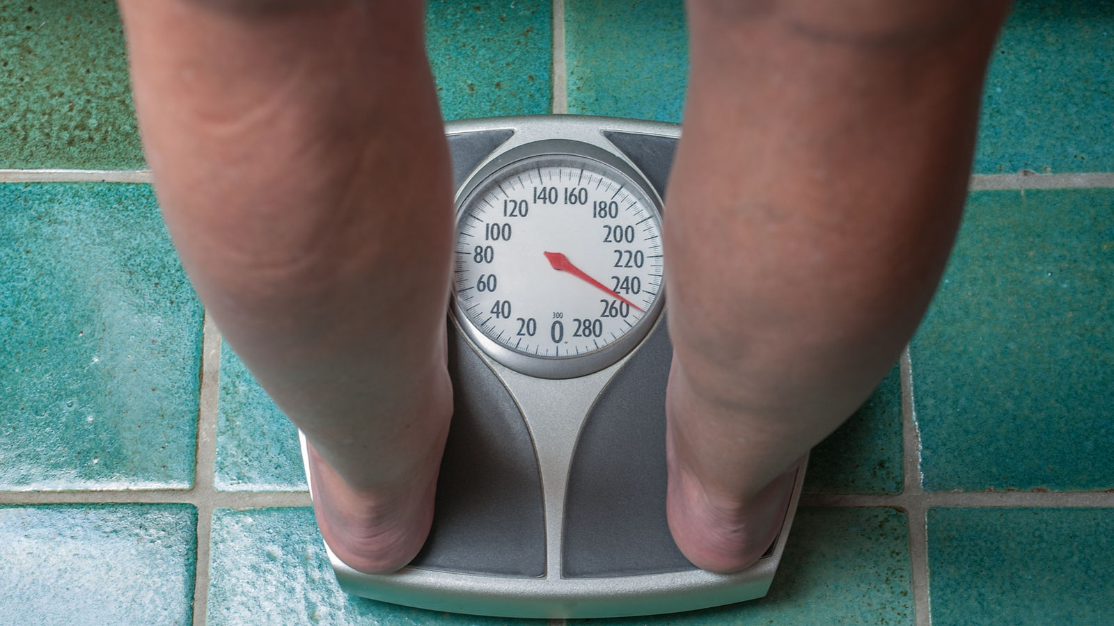 A severely overweight person weighing herself or himself on a bathroom scale