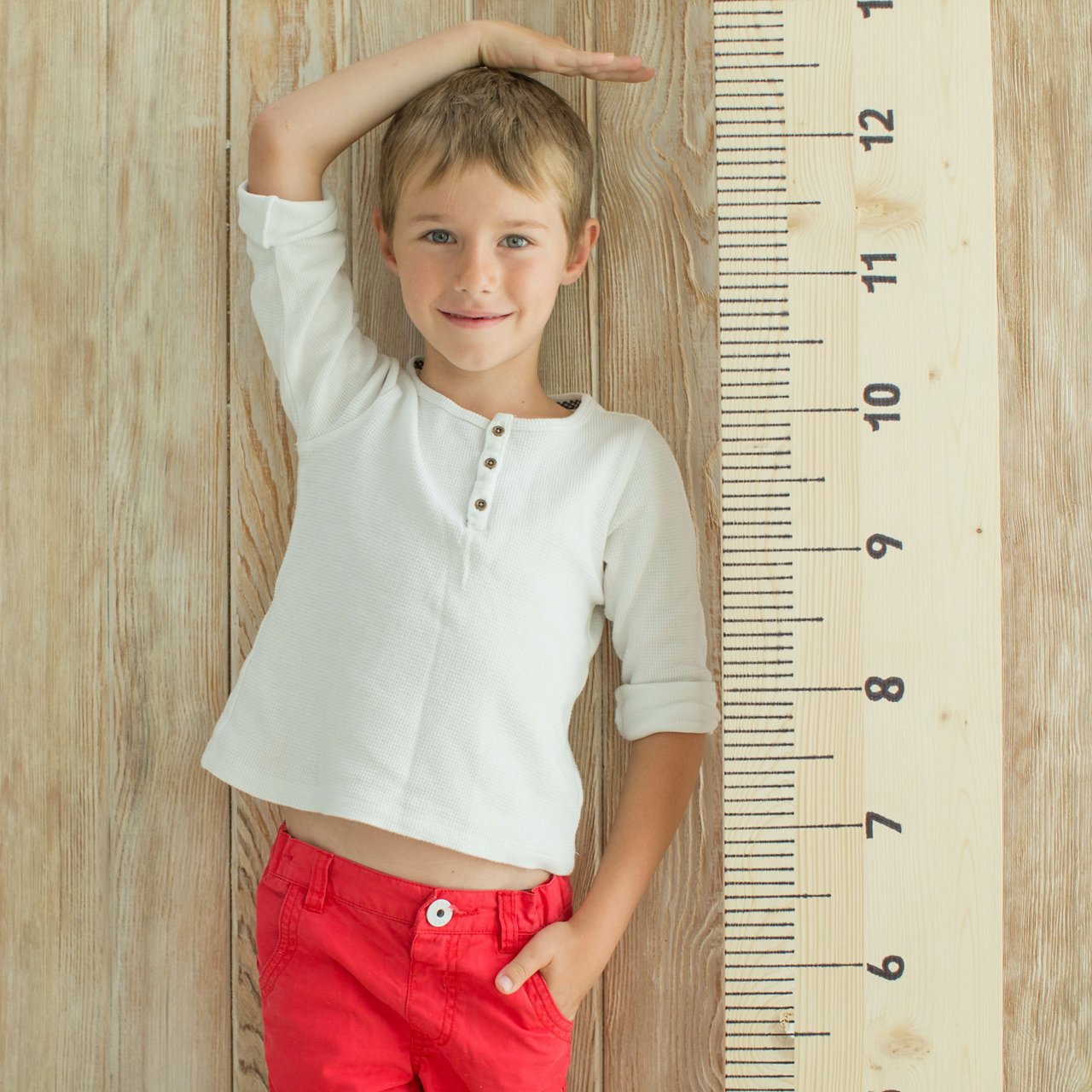 Junge steht neben einem übergroßen Lineal und misst seine Körpergröße