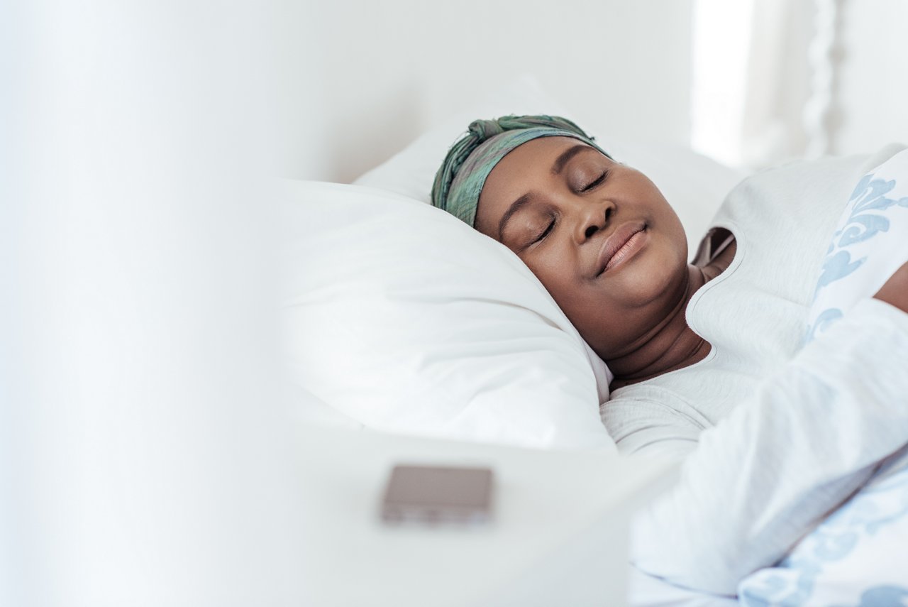 Young African woman wearing a headscarf fast asleep under the duvet of her bed at home in the early morning