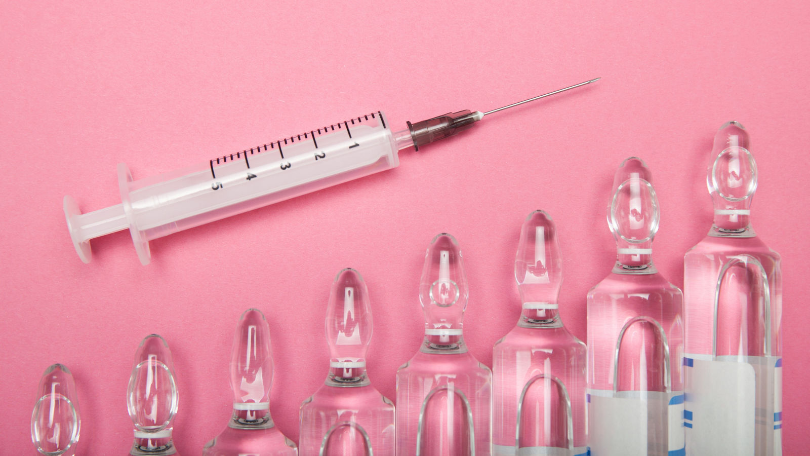 Increasing dependence on injections of hyaluronic acid, botox and collagen. Syringe and ampoules on a pink background.