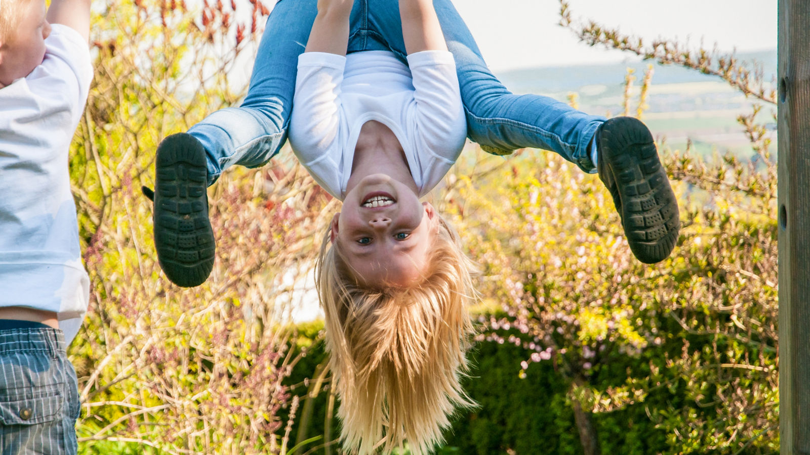Lachendes Mädchen turnt an der Reckstange, ist draußen und zeigt fröhliches Selbstbewusstsein