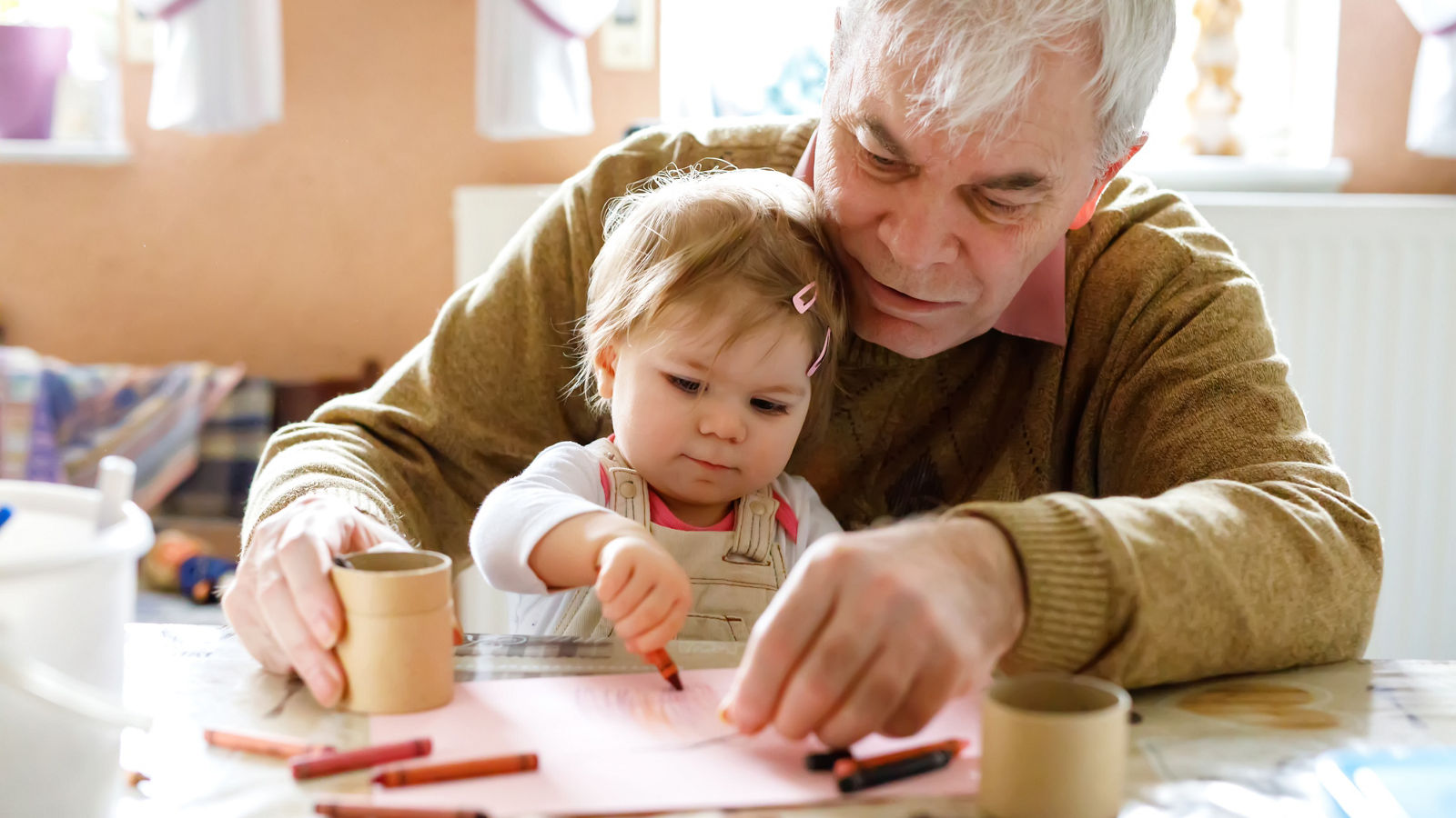 Cute little baby toddler girl and handsome senior grandfather painting with colorful pencils at home. Grandchild and man having fun together
