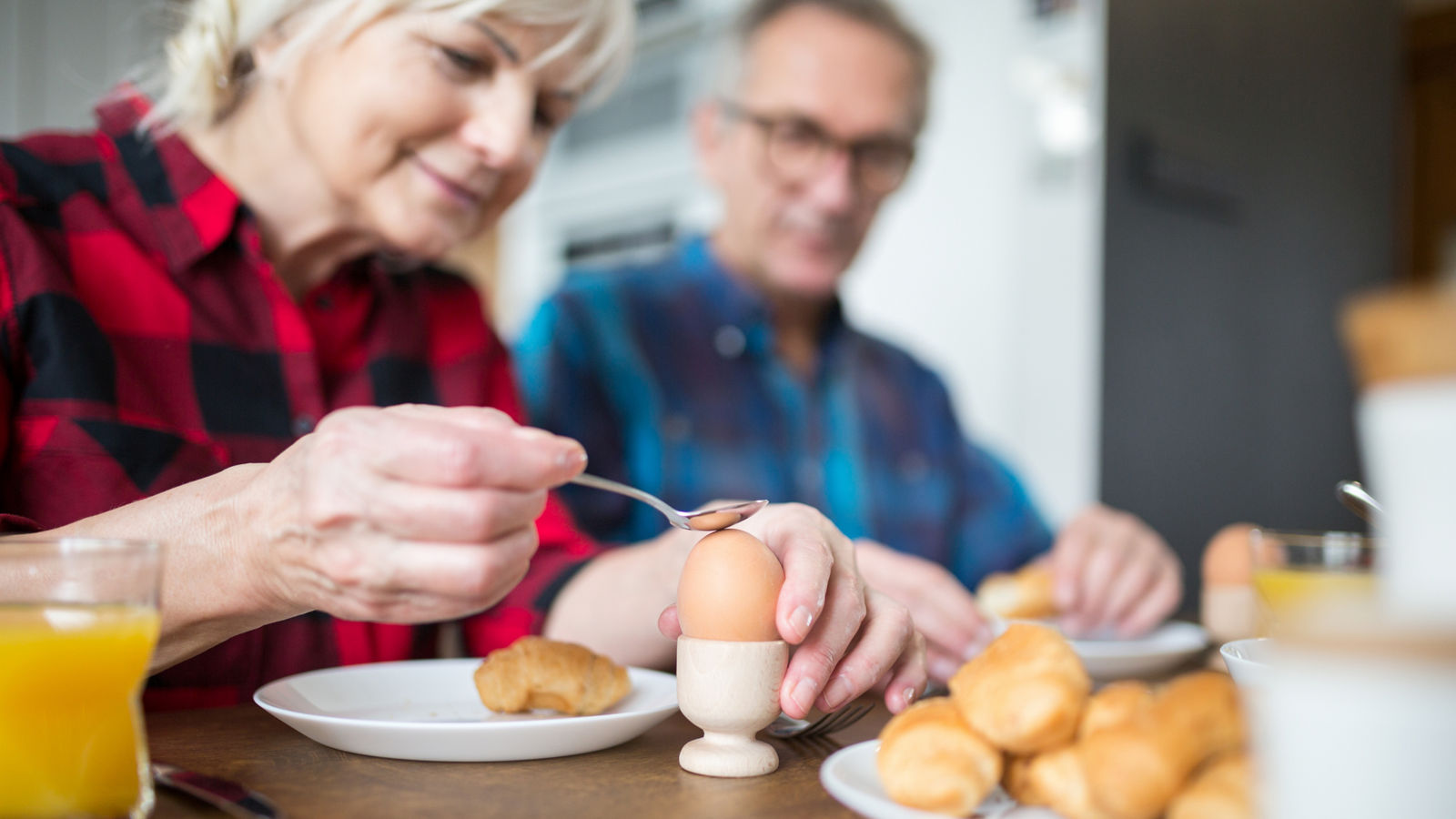 Senior woman breaking boiled egg for breakfast