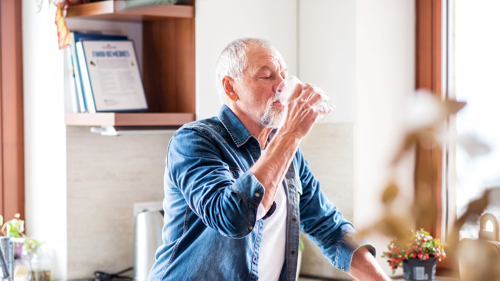 Senior man drinking water in the kitchen.