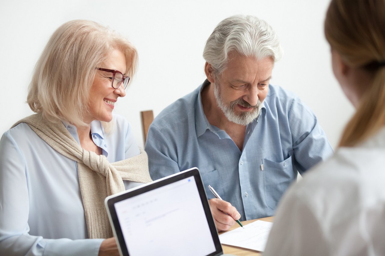 Happy senior couple about to sign document at meeting with financial advisor, older man agrees to put signature on contract making investment purchase, taking insurance, aged family in travel office