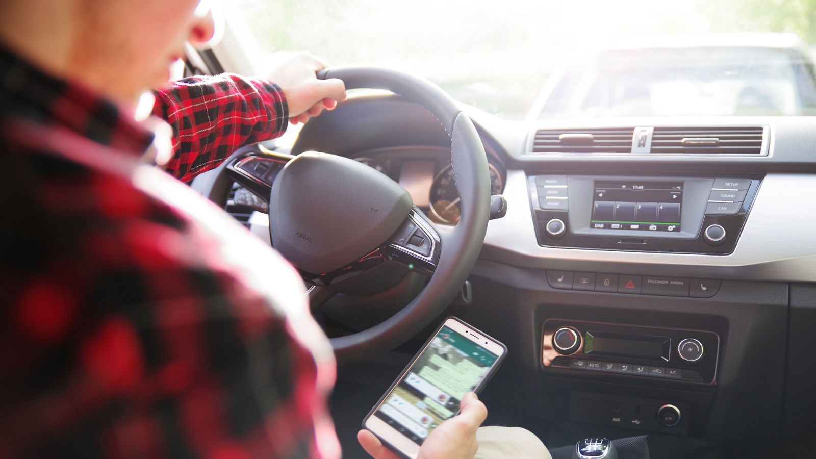 Mann schaut während der Fahrt auf sein Handy 