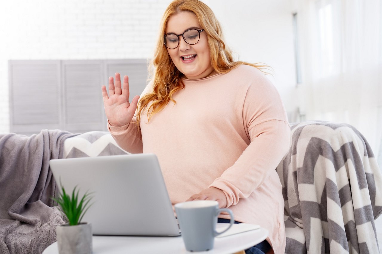 Glückliche Frau arbeitet an ihrem Laptop und winkt in die Kamera