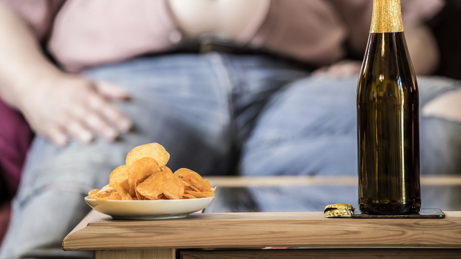 ein dicker Mann sitzt an einem Tisch auf dem Bier und Kartoffelchips stehen