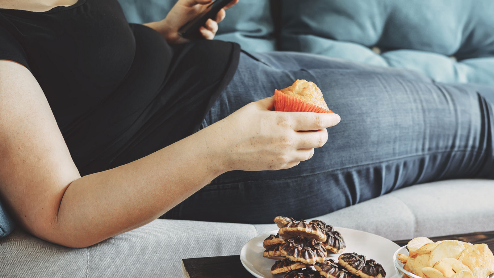 Overweight woman laying on sofa eating sugary food
