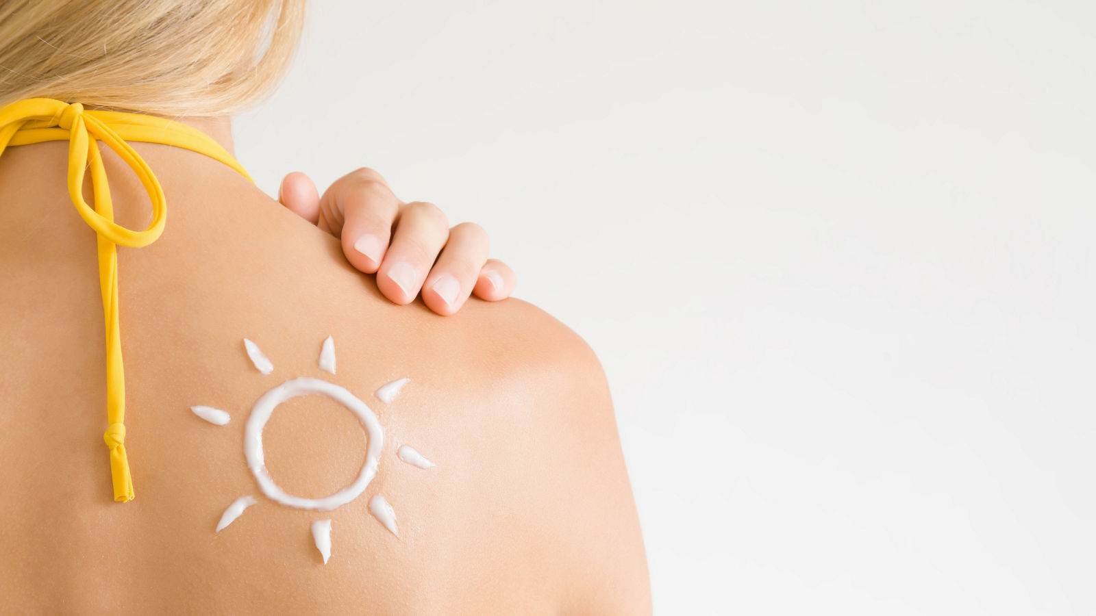 Sun shape created from sunscreen lotion on young woman's back. Skin protection. Safety sunbathing concept. Copy space. Empty place for text on light gray background.
