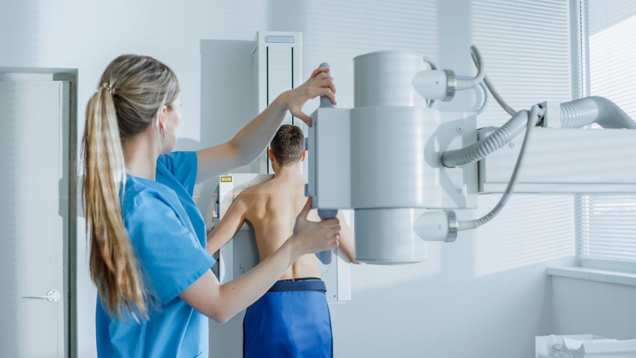 In the Hospital, Man Standing Face Against the Wall While Medical Technician Adjusts X-Ray Machine For Scanning. Scanning for Fractures, Broken Limbs, Chest, Cancer or Tumor. Modern Hospital with Technologically Advanced Medical Equipment.