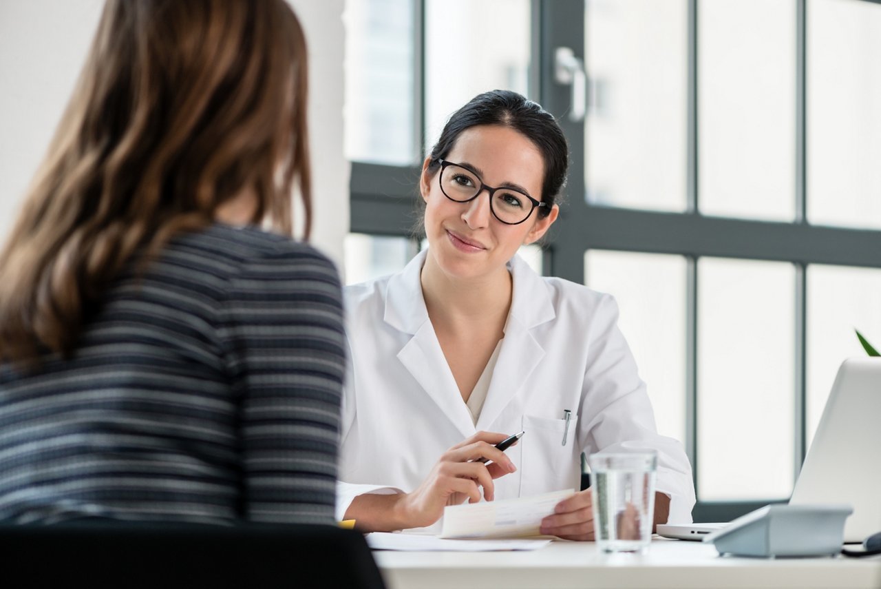 Female physician listening to her patient during consultation while sitting down in the office of a modern medical center