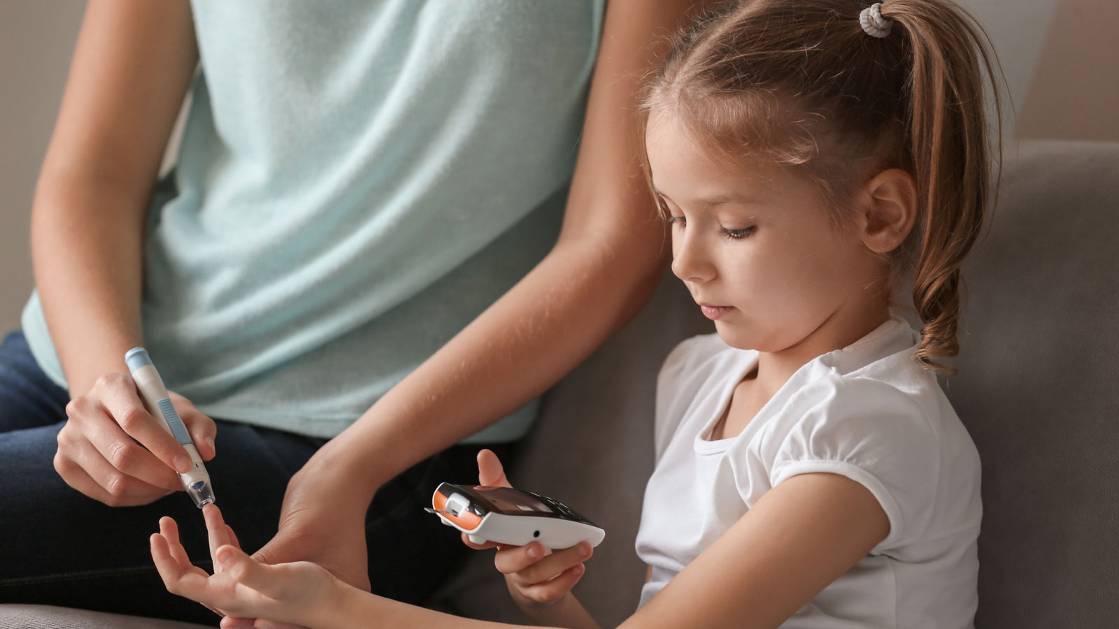 Woman and her diabetic daughter with lancet pen and digital glucometer taking blood sample at home