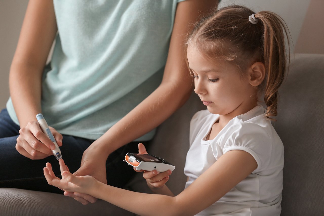 Woman and her diabetic daughter with lancet pen and digital glucometer taking blood sample at home