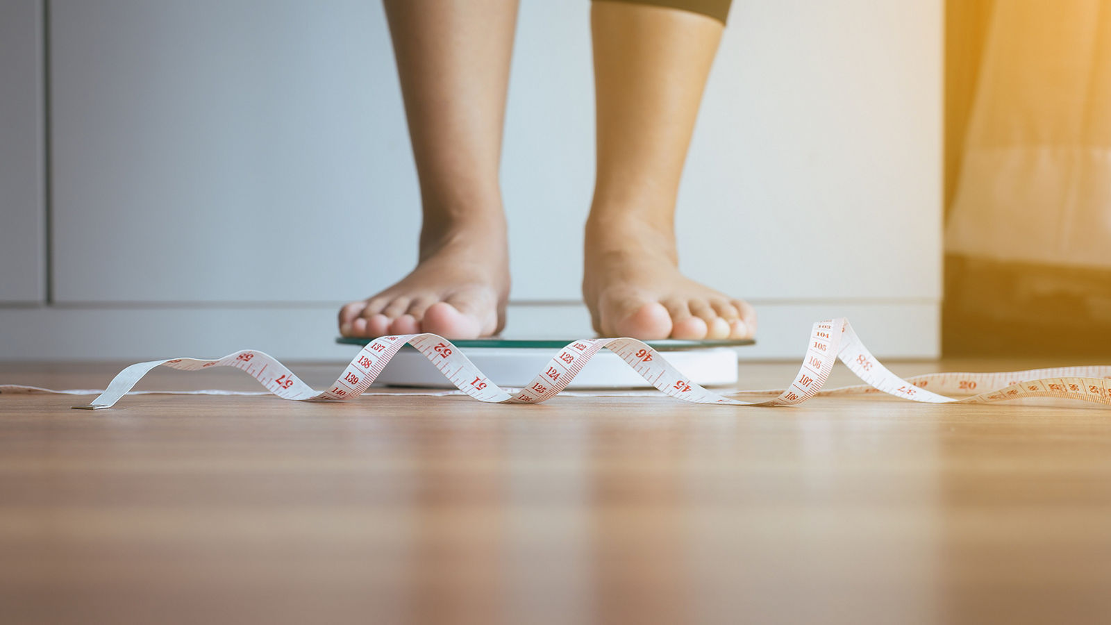 Woman feet standing on weigh scales with tape measure in foreground,Weight loss,Body and healthcare concept,Woman feet standing on weigh scales with tape measure in foregro