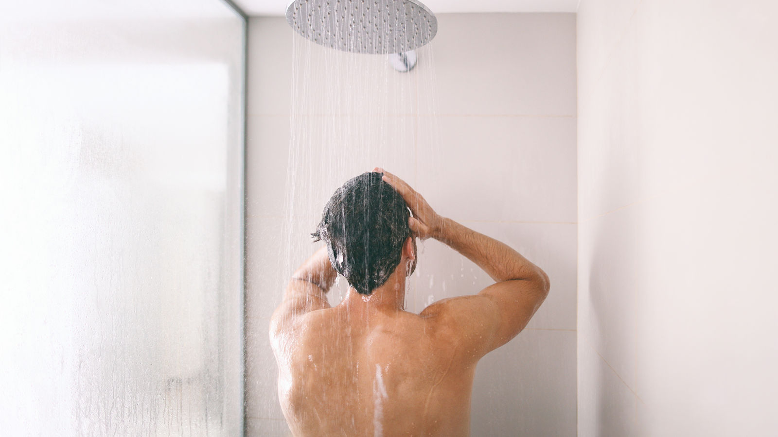 Man taking a shower washing hair with shampoo product under water falling from luxury rain shower head. Morning routine luxury hotel lifestyle guy showering. body care hygiene.