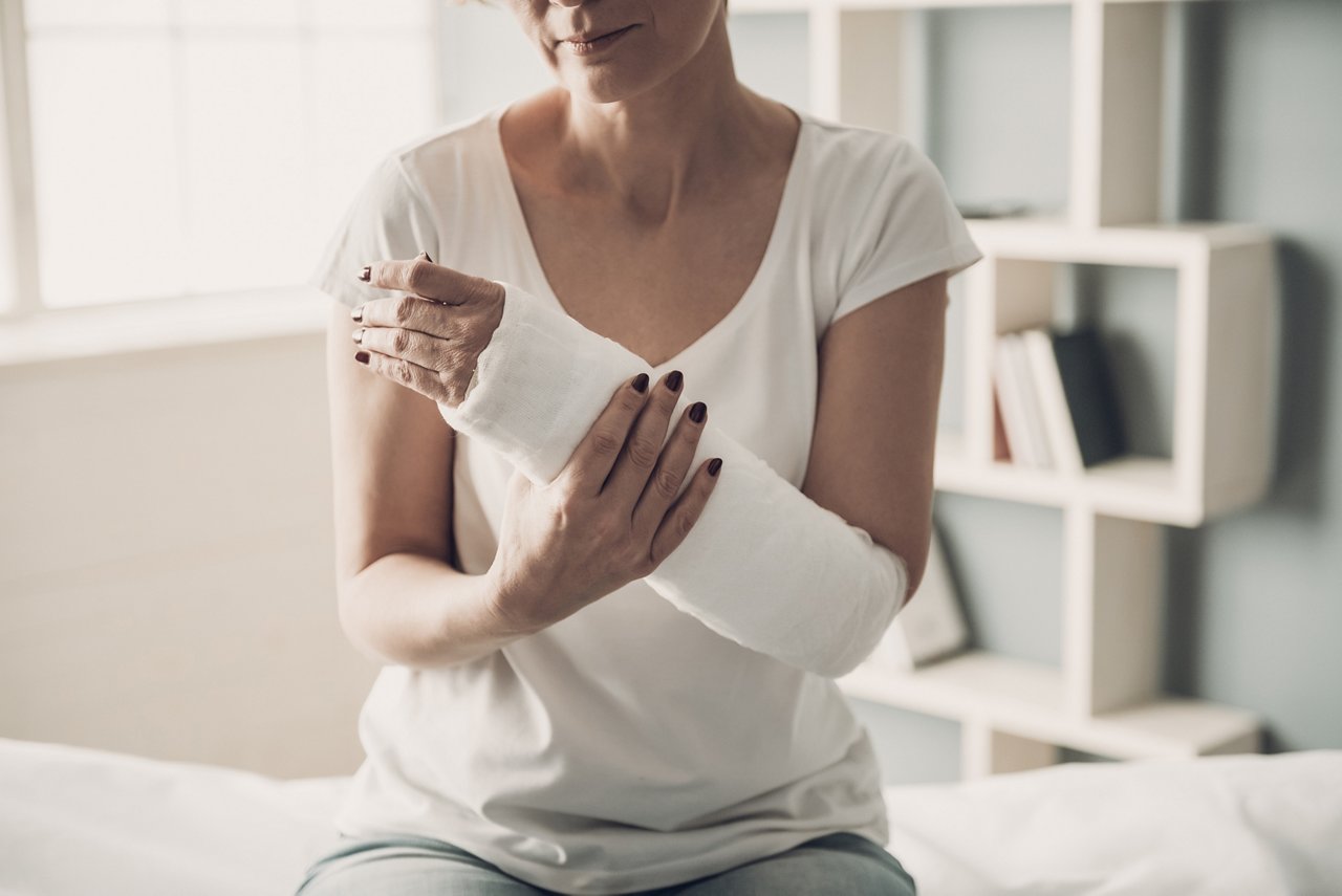 Close-up of Female Broken Arm in Plaster Cast. Caucasian Injured Woman in White T-Shirt Sitting and Holding Wrist in Gypsum Bandage with Physical Pain in Fractured Bone. Health Care concept