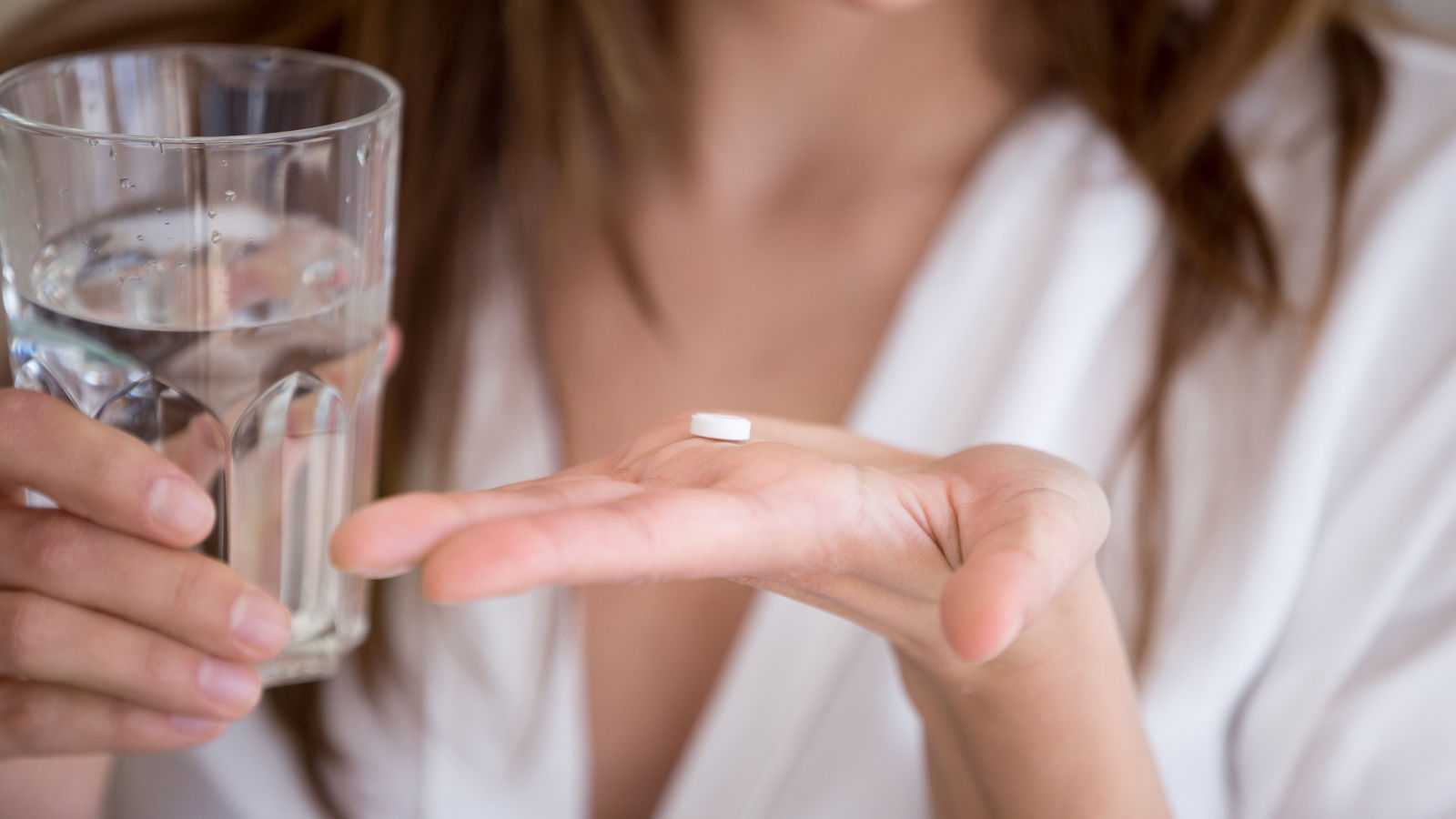 Woman holding pill and glass of water, close up view