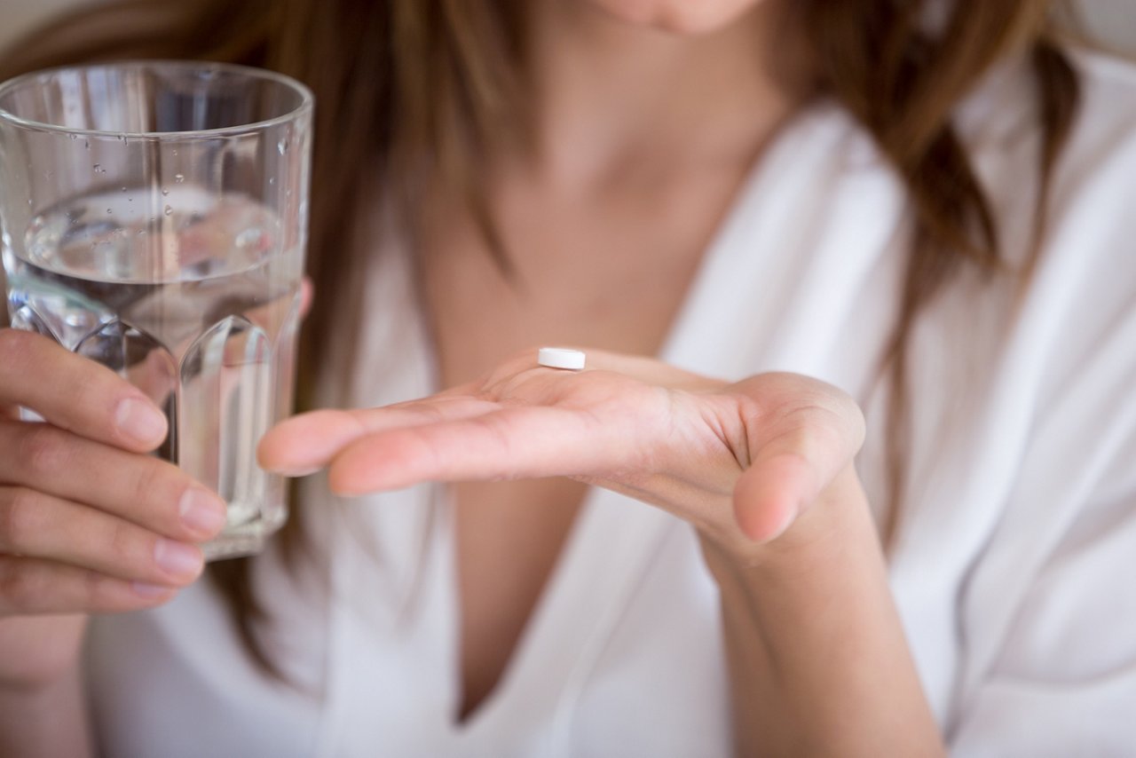Woman holding pill and glass of water in hands taking emergency medicine, supplements or antibiotic antidepressant painkiller medication to relieve pain, meds side effects concept, close up view