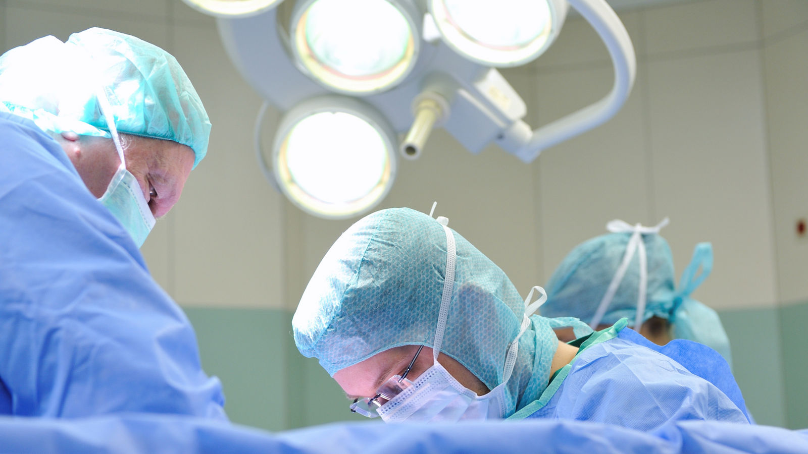 Operateure stehen am OP-Tisch mit OP-Kleidung und Masken